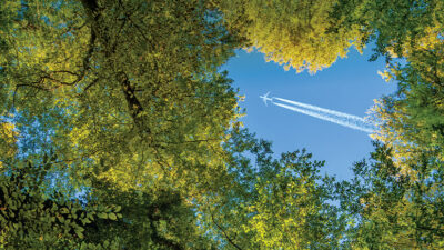 aircraft with jet trails flying over trees