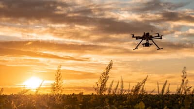 Drone in flight over field at sunset.